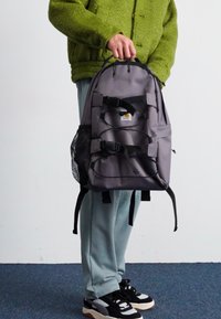 Gray backpack with adjustable straps, front buckles, and a mesh side pocket. The material is durable with a smooth texture.