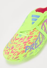 Chaussures de football jaune-vert vif avec un imprimé léopard rose, présentant une pointe arrondie et un logo d'accent bleu, maintenues par une sangle élastique.