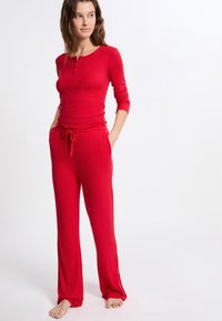 Rode, lange mouwen top met henley hals en bijpassende trekkoordbroek. Zacht, lichtgewicht materiaal met een comfortabele pasvorm en zijzakken.