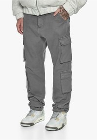 Grå cargo bukser i stof med flere lommer, parret med grå og hvide sneakers med mesh- og læderdetaljer.