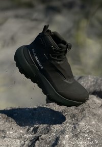 Black hiking shoe with a high ankle design, waterproof GORE-TEX material, textured upper, and a rugged sole, elevated above rocky surface.