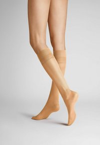 Knielange, durchsichtige Kompressionsstrümpfe in einem natürlichen Beige mit einer glatten Textur und einem elastischen Bund oben, mit dezentem Branding.