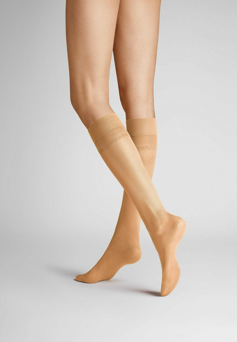 Knielange, durchsichtige Kompressionsstrümpfe in einem natürlichen Beige mit einer glatten Textur und einem elastischen Bund oben, mit dezentem Branding.