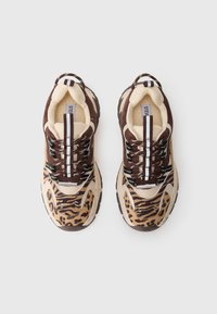 Un paio di sneaker con stampa animale beige e marrone, con lacci bianchi e neri su uno sfondo bianco.