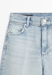 Ceinture de pantalon en jean bleu clair avec bouton avant, passants de ceinture et détails de couture des poches sur fond blanc.