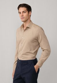 Lichtbruin overhemd met knopen van gestructureerde stof, voorzien van een klassieke kraag en lange mouwen, gecombineerd met donkere geruite broek.