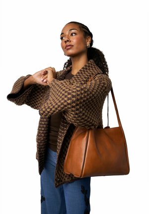 Rjavi pleteni kardigan z teksturiranim vzorcem, rjava usnjena torbica, modre hlače s cvetličnim vezenjem. Enostavne, strukturirane oblike in barve.