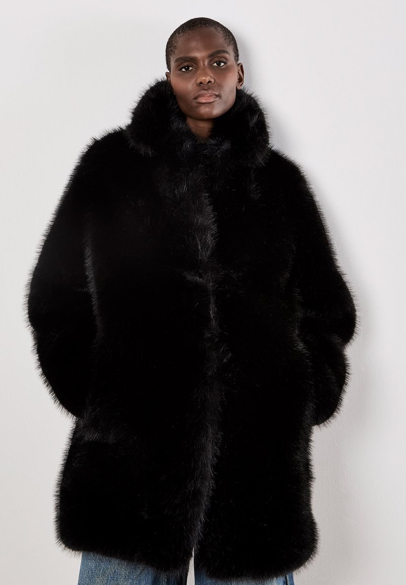 Cappotto in pelliccia sintetica nera con colletto alto, silhouette oversize e texture morbida. Presenta una chiusura frontale nascosta e maniche lunghe.