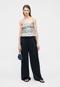 Γυναίκα που φοράει αμάνικο μπλουζάκι με γαλάζιο λουλουδάτο σχέδιο, φαρδιές μαύρες παντελόνες, μαύρα σανδάλια και κρατά μια μικρή μπλε τσάντα με σχέδιο.