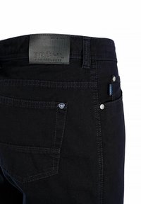 Czarne spodnie dżinsowe z teksturowanym paskiem z metką, licznymi kieszeniami, srebrnymi elementami metalowymi oraz kontrastującymi detalami szwów.