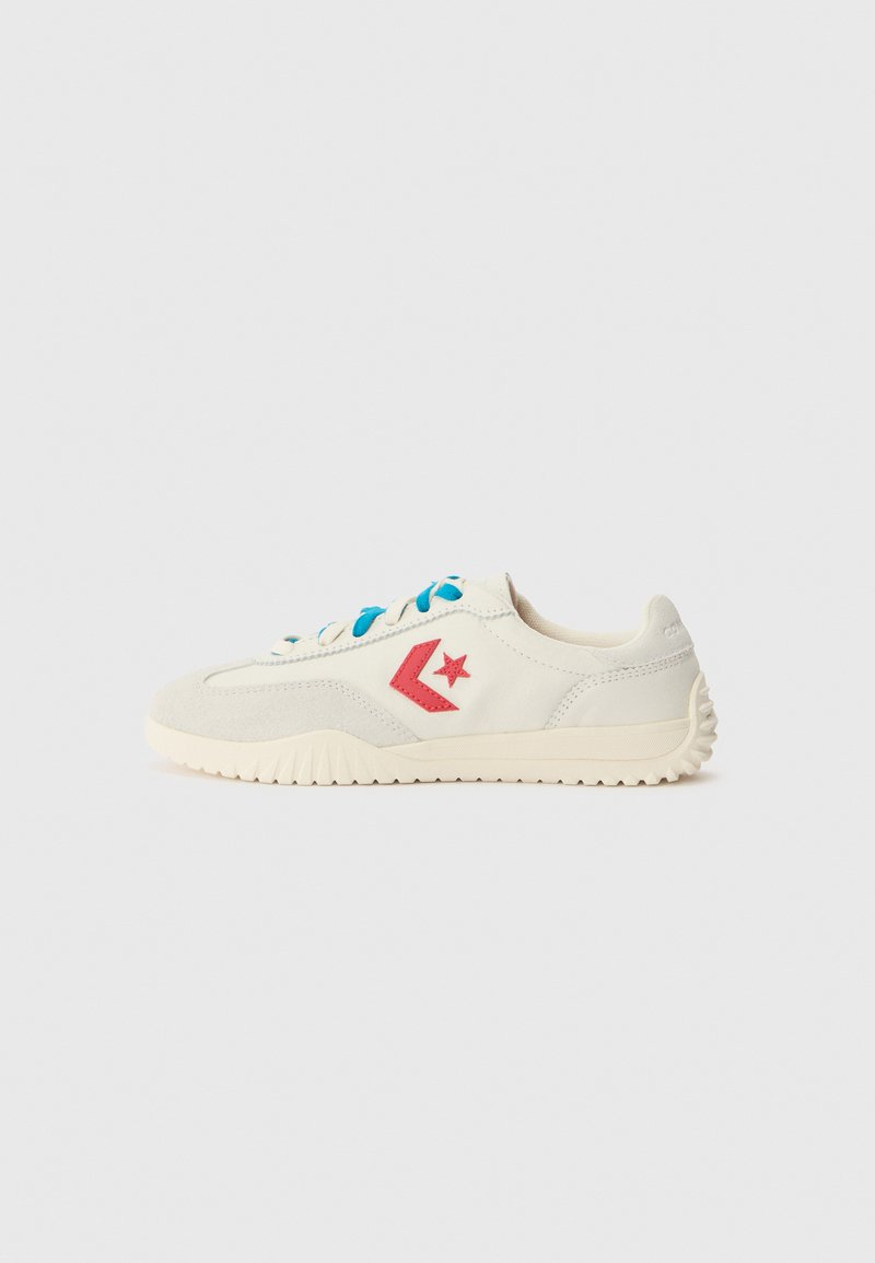 Tenis alb cu logo în formă de stea roșie, accente din suede gri deschis, șireturi albastre și talpă din cauciuc texturat; design cu profil scăzut și formă rotunjită.