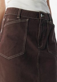 Brun denimkjol med en åtsittande siluett, prydd med vit sömnad och två bakfickor. Tyget har en slät yta.