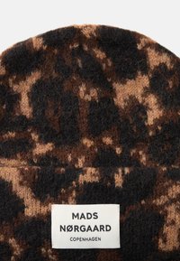 Gorro de malha castanho com padrão de estampado de leopardo, apresentando uma textura suave e um etiqueta de marca visível com "MADS NØRGAARD COPENHAGEN."