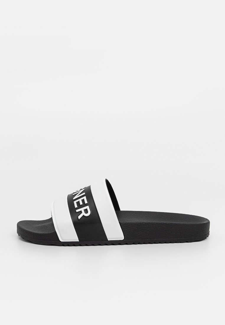 Schwarze und weiße Slidesandale mit zwei breiten Riemen. Der obere Riemen ist schwarz mit weißem Text, während die Sohle aus strukturiertem schwarzem Gummi besteht.