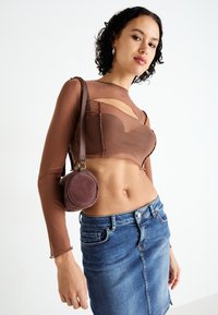 Brown sheer long-sleeve top with cut-outs over a fitted brown bodice, paired with a denim mini skirt and a round brown bag.