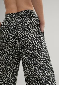 Czarno-białe spodnie w print z luźnym krojem, z elastyczną talią i bocznymi kieszeniami, prezentujące odważny, abstrakcyjny wzór.