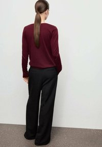 Burgundy long-sleeve top paired with black wide-leg trousers. The outfit emphasizes a fitted silhouette and smooth textures.