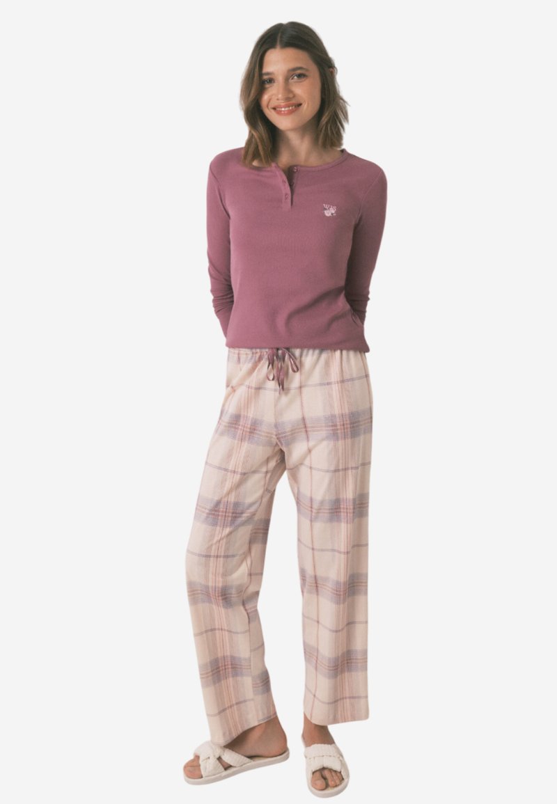 Dlouhý rukáv fialového topu s detaily knoflíků, v kombinaci s lehkými krémovými kalhotami s kostkovaným vzorem. Model nosí světlé slip-on obuv.