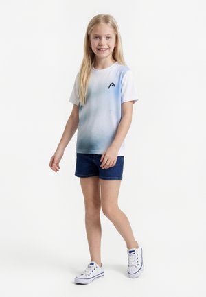 Šypsanti mergina su ilgais blondinų plaukais, dėvinti mėlynos ir baltos gradientinės spalvos marškinėlį, tamsiai mėlynas trumpas kelnes ir baltus sportbačius, einanti pirmyn.