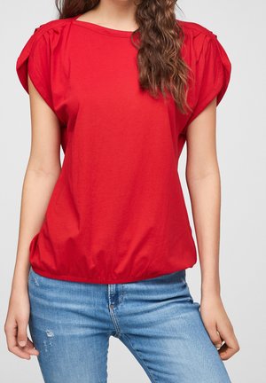 Haut rouge à manches courtes en coton doux, avec un col froncé et un ourlet peplum. Assorti à un jean bleu clair usé.