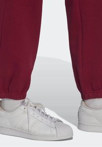Burgunder joggers med elastiske manchetter, parret med hvide lædersneakers, der har en tekstureret overdel og klassisk tre-stribe design.