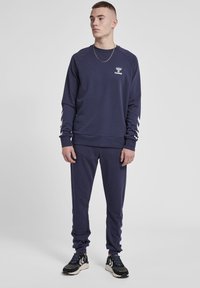 Navy Sweatshirt- und Hosen-Set aus weichem Material mit geripptem Saum. Mit weißen Chevron-Streifen an den Ärmeln und einem Logo auf der Brust.