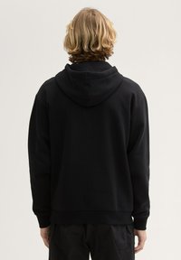 Sudadera con capucha negra, de tejido texturizado, corte relajado y puños de canalé. Incluye una capucha amplia y un bolsillo tipo canguro.