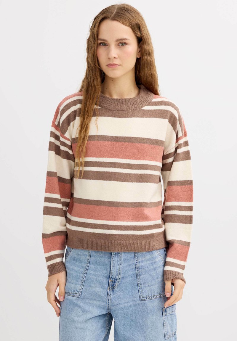 Suéter a rayas en colores marrón claro, coral y crema. Cuello redondo, textura suave, mangas largas y puños y dobladillo acanalados. Combinado con jeans azules.