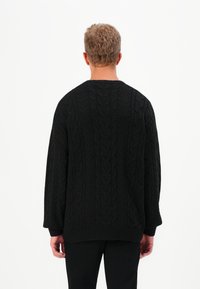 Maglione nero a trecce con scollo rotondo, vestibilità oversize e polsini a costine. Il motivo testurizzato presenta design a treccia verticali.