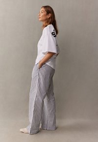 Vit oversized t-shirt med svart text, kombinerad med grå och vita vertikalt randiga vida byxor. Avslappnat tyg med fickor.
