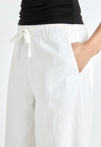 White linen pants with an elastic waistband and drawstring. Features side pockets and a slightly textured fabric for breathability.