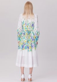 Robe fleurie blanche avec des motifs bleus, jaunes et verts. Présente des manches bouffantes longues, une taille cintrée et une jupe midi.