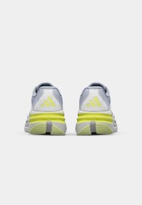 Baskets de sport gris clair avec des accents jaunes, fabriquées en tissu respirant. Équipées d'une semelle rembourrée et d'un col matelassé pour le confort.