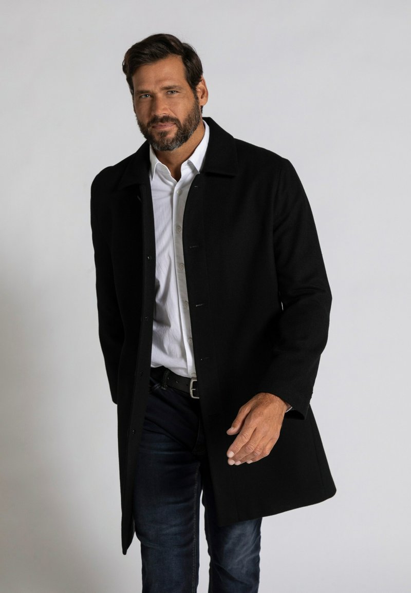 Abrigo de lana negro con cuello, cierre de botones y bolsillos laterales, llevado sobre una camisa blanca y jeans azules. Textura suave, corte entallado.