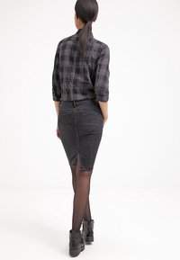 Svart rutigt skjorta med uppvikta ärmar, kombinerad med en åtsittande svart denimkjol med slits bak och två bakfickor. Svarta ankelboots.