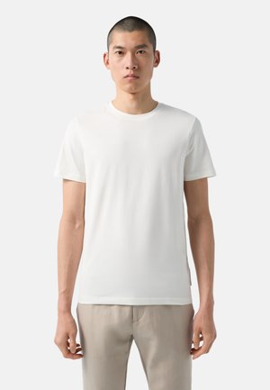 Hvid bomulds t-shirt med korte ærmer og rund halsudskæring. Har et subtilt præget logo på brystet. Glat tekstur og tætsiddende form.