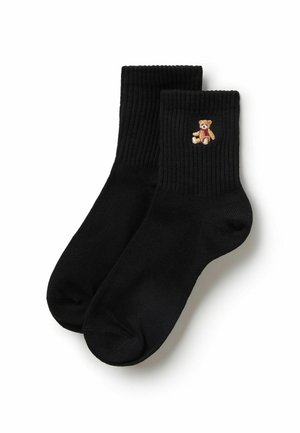 Paar schwarze gerippte Socken mit kleinem besticktem Teddybären, der einen roten Schal trägt, an der Seite nahe dem oberen Bündchen.