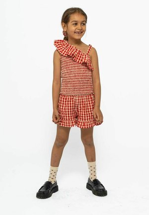 Rød og hvid ternet outfit med ruffled top med én skulder og matchende shorts. Sorte sko og knæhøje sokker med hjerte mønster.