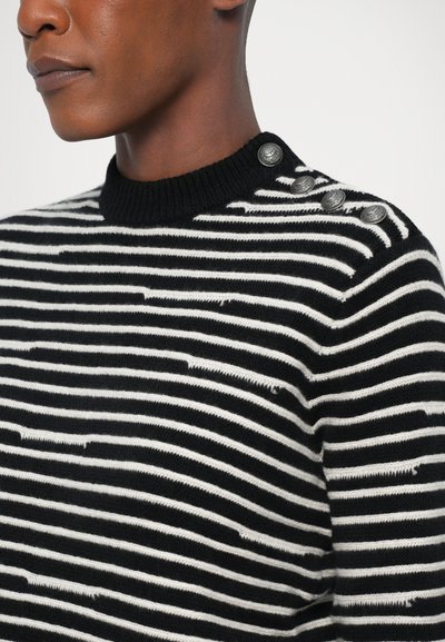 Maglione a righe bianche e nere con collo rotondo, caratterizzato da dettagli in metallo su una spalla e una trama in stile distressed.