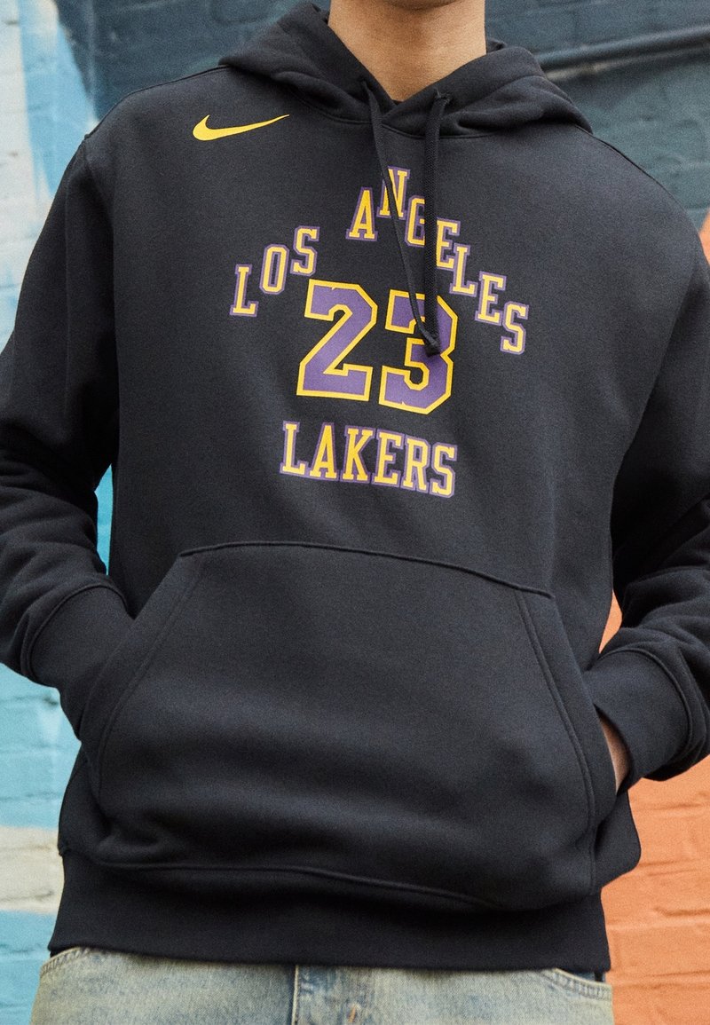 Un sweat à capuche noir en matériaux polaires, doté d'une poche kangourou, d'un logo Nike en jaune et d'un graphique des Los Angeles Lakers en violet et jaune.
