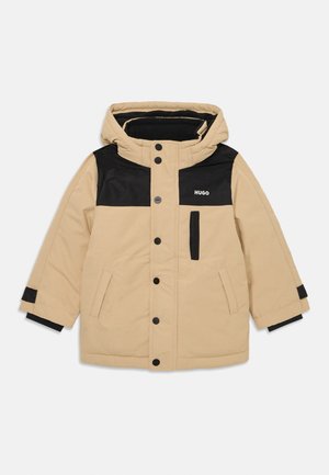 Beige Daunenjacke mit einem schwarzen oberen Abschnitt, Kapuze und Druckknopfverschluss. Verfügt über seitliche Taschen und kontrastierende schwarze Bündchen.