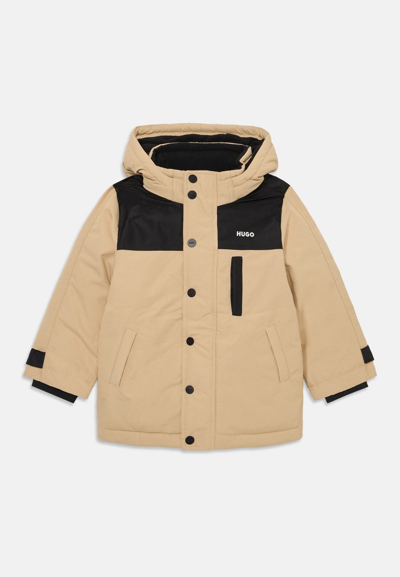Casaco puffer bege com uma secção superior preta, capuz e fecho de botão de pressão. Apresenta bolsos laterais e punhos pretos contrastantes.