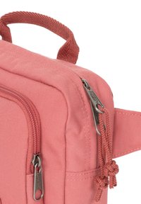 Sac en tissu rose avec une surface texturée, doté d'une poignée supérieure, de deux zips et d'accents en nœuds décoratifs sur les tirettes des zips.
