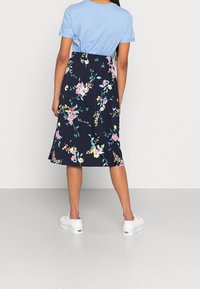 Chemise bleu à manches courtes associée à une jupe bleu marine longueur genou arborant un motif floral coloré, agrémentée de baskets blanches.