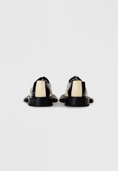 Chaussures en cuir noir et crème avec une finition texturée, bout rond et semelle en caoutchouc. Comprend des zips latéraux et une languette à l'arrière.