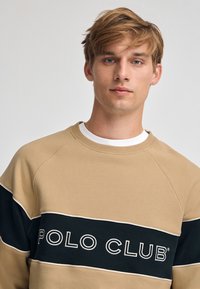 Felpa beige con pannello blu navy riportante il testo "POLO CLUB". Tessuto morbido, collo a costine e maniche raglan. Design minimalista.