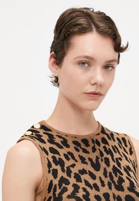 Brun uten ermer topp med svart leopardmønster, teksturert strikkemateriale og gullknappdetaljer på skulderen.