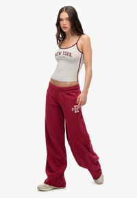 Grijze katoenen tanktop met "NEW YORK" in bordeauxrood gedrukt, gecombineerd met losse bordeauxrode joggingbroek met een wit logo. Zachte textuur.