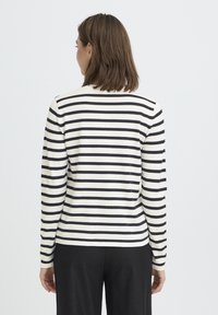 Pull rayé crème et noir, avec manches longues, texture côtelée et encolure arrondie. Porté avec un pantalon noir.