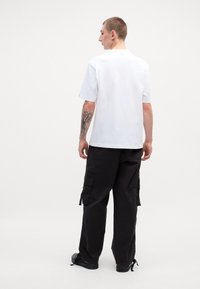 Hvid bomulds t-shirt med korte ærmer, parret med sorte cargo bukser med sidelommer og lynlåse. Sorte sneakers fuldender outfittet.